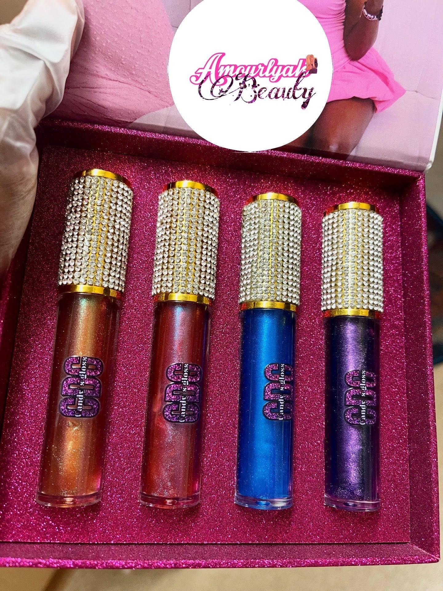Set of four lip glosses in a pink case with 'Amenity Beauty' branding.